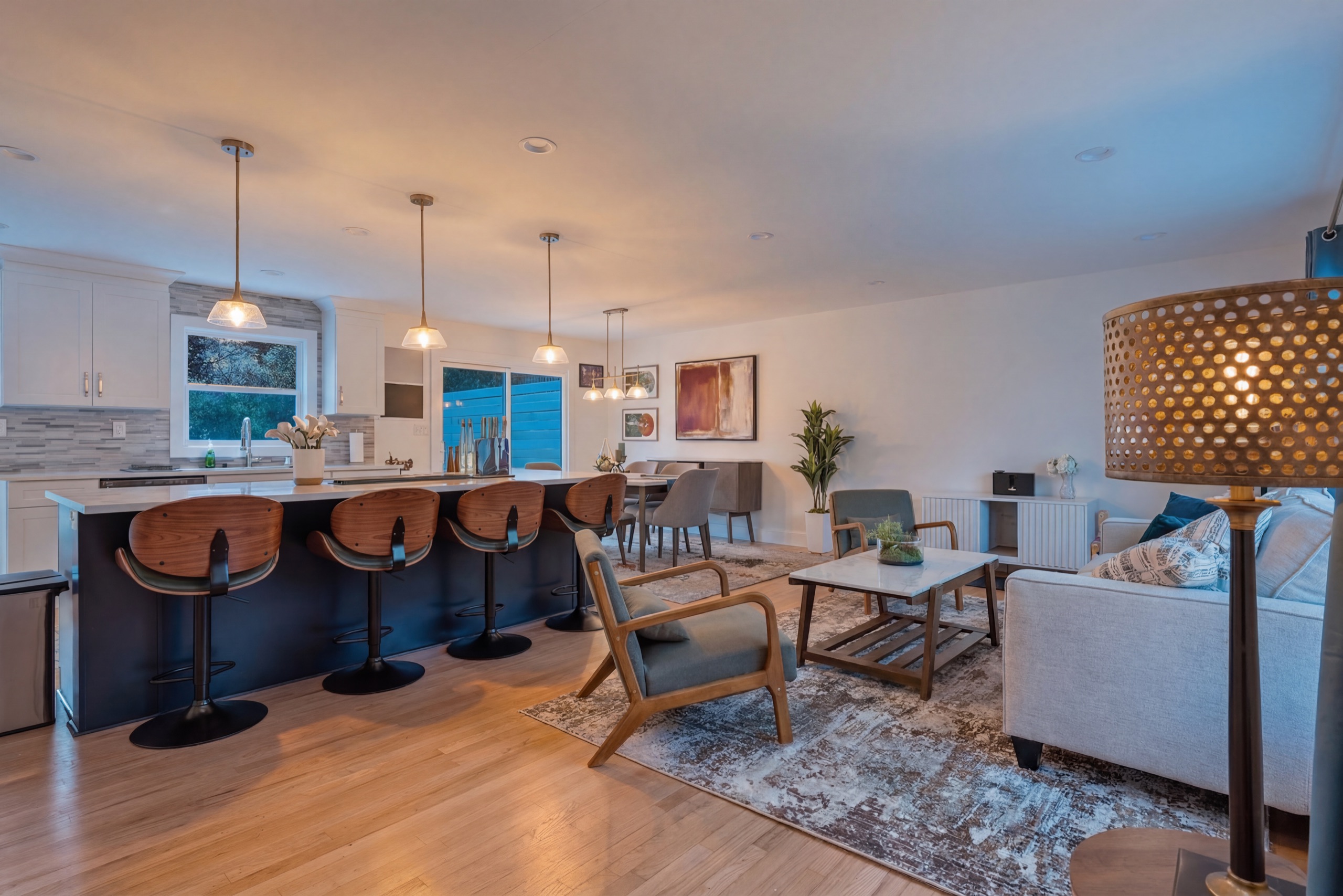 Same kitchen and living room in warm evening light with fixtures glowing